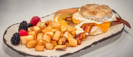 Un plato de desayuno con sándwich de galleta, huevos fritos, tocino, patatas ralladas y frutos rojos.