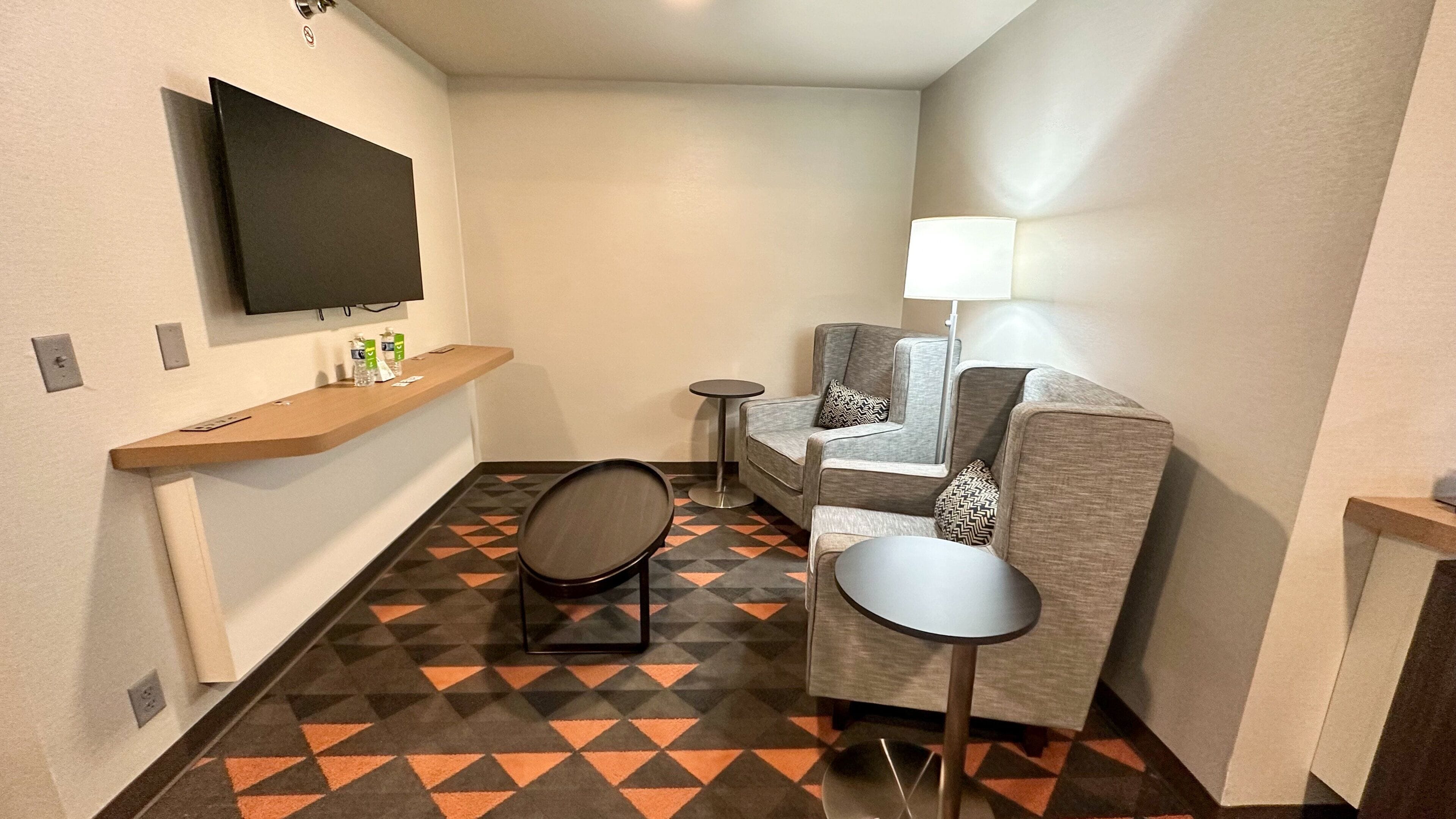A compact hotel room with a flat-screen TV, a sofa, a small table, and a lamp.