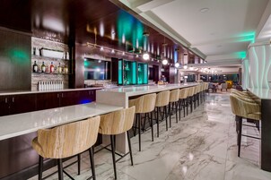 A modern bar area with a long counter, multiple stools, and a variety of bottles.