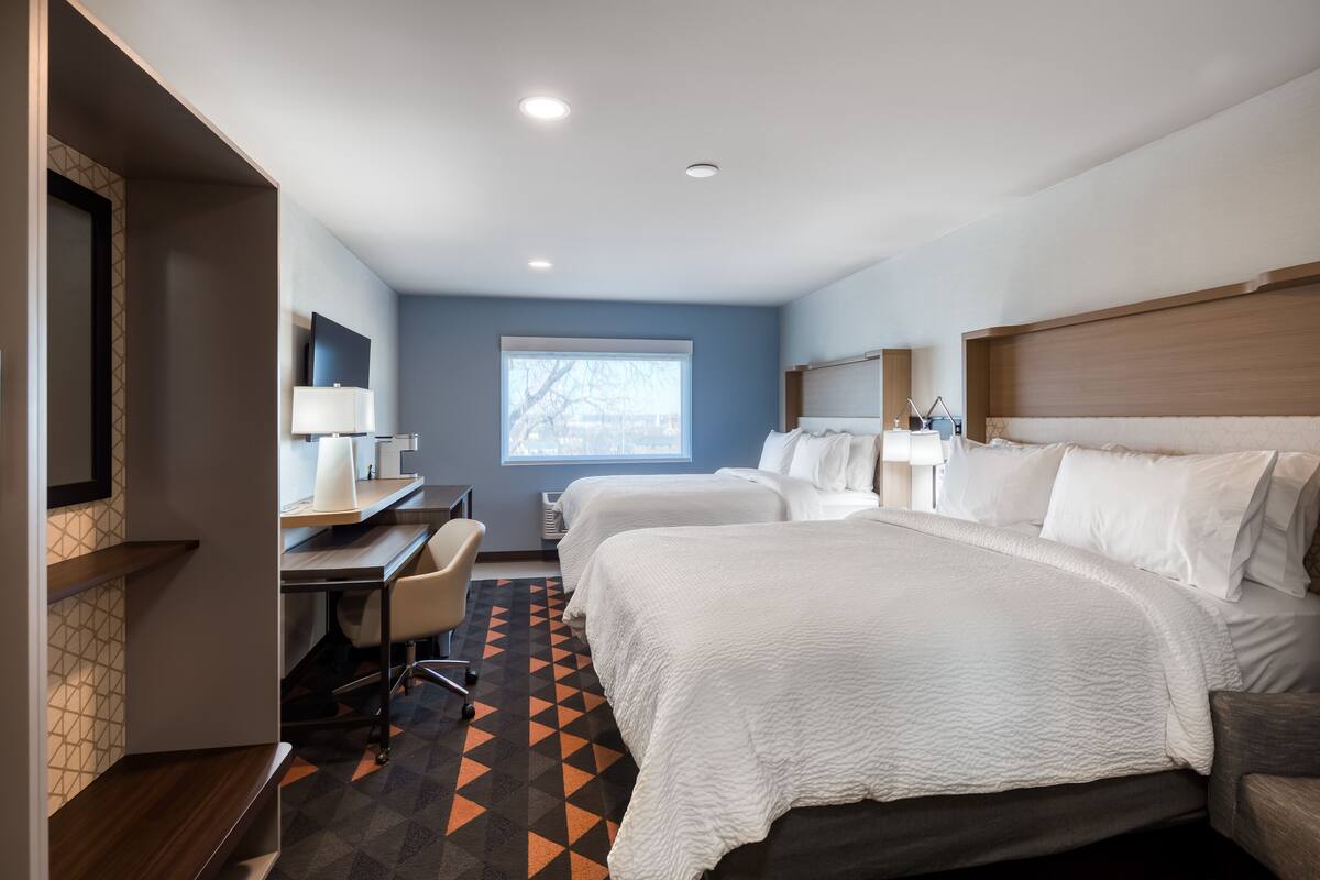Een hotelkamer met twee bedden, een bureau, een stoel en een groot raam.
