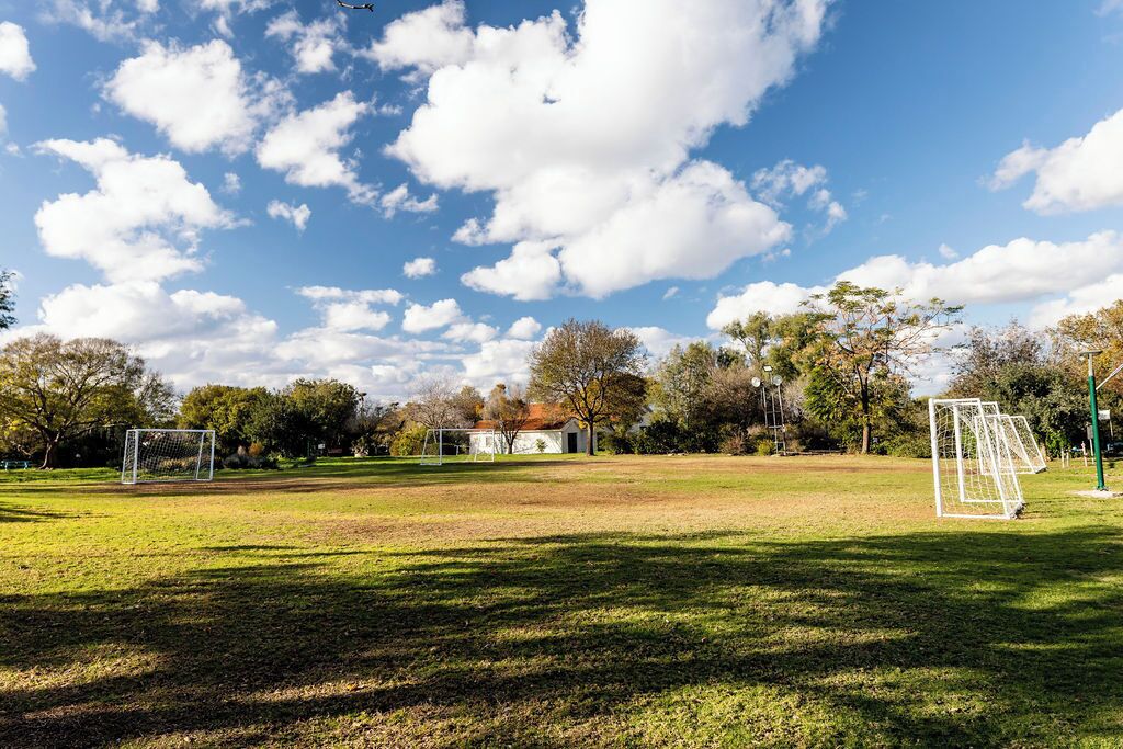 Un terrain herbeux avec deux buts de football, des arbres et un bâtiment en arrière-plan.