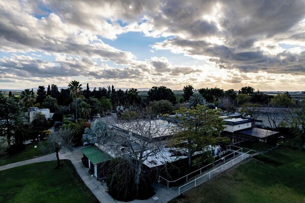 An aerial view of a residential area with a large building, surrounded by trees and a clear sky. - Nes Ammim Hotel (Mateh Asher)