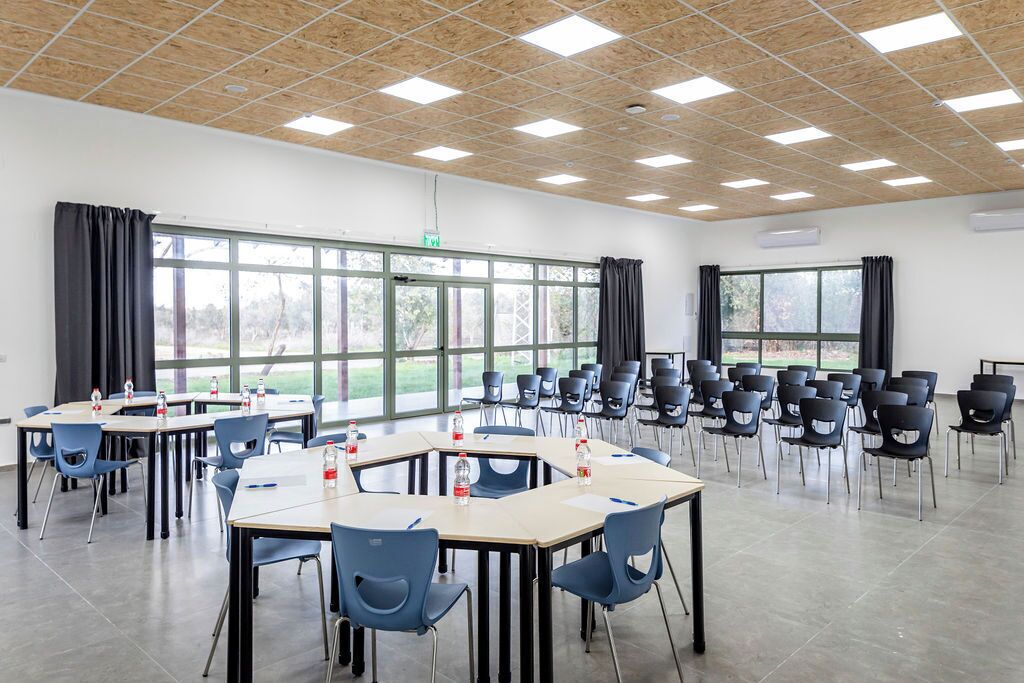 Une salle de conférence équipée de tables et de chaises, dotée de grandes fenêtres et d’un plafond en bois.