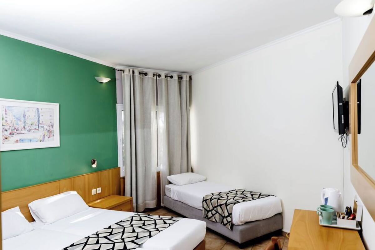 A hotel room with two beds, a desk, a chair, a painting on the wall, and a window with curtains.