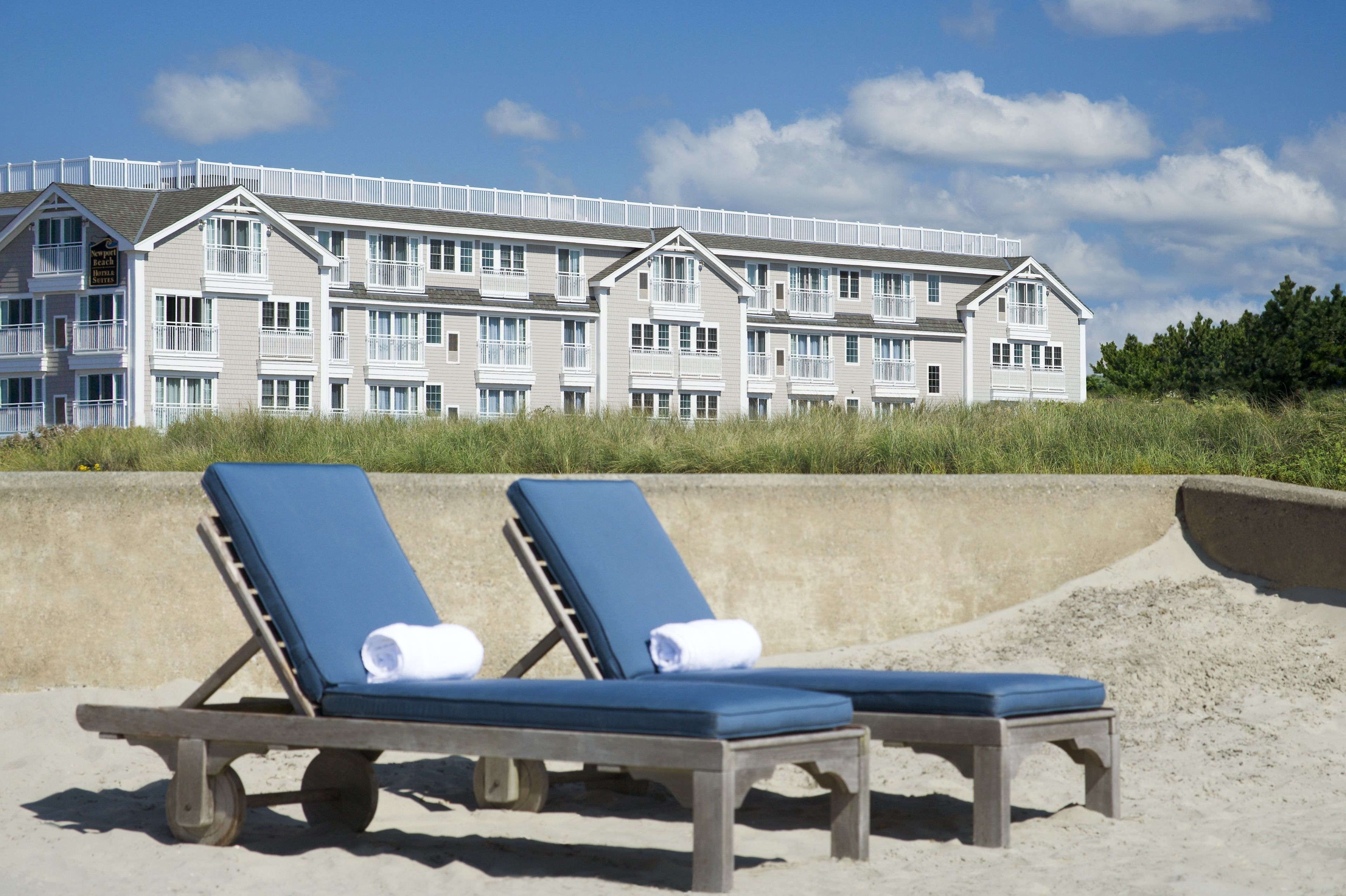 Un hôtel situé en bord de mer, avec une rangée de chaises longues bleues et une barrière en béton.