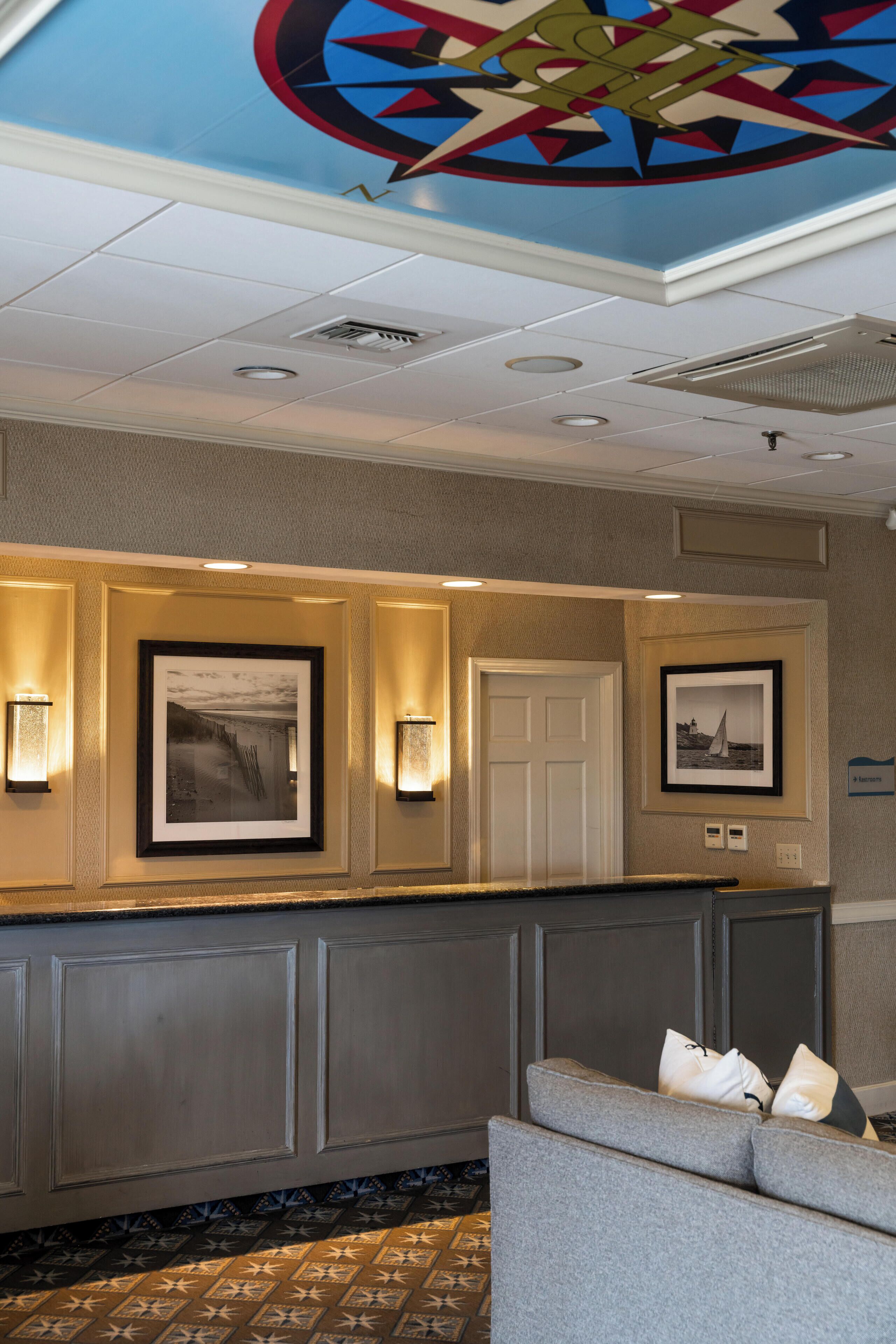 A hotel lobby with a reception desk, framed artwork, wall sconces, a door, and a patterned carpet.