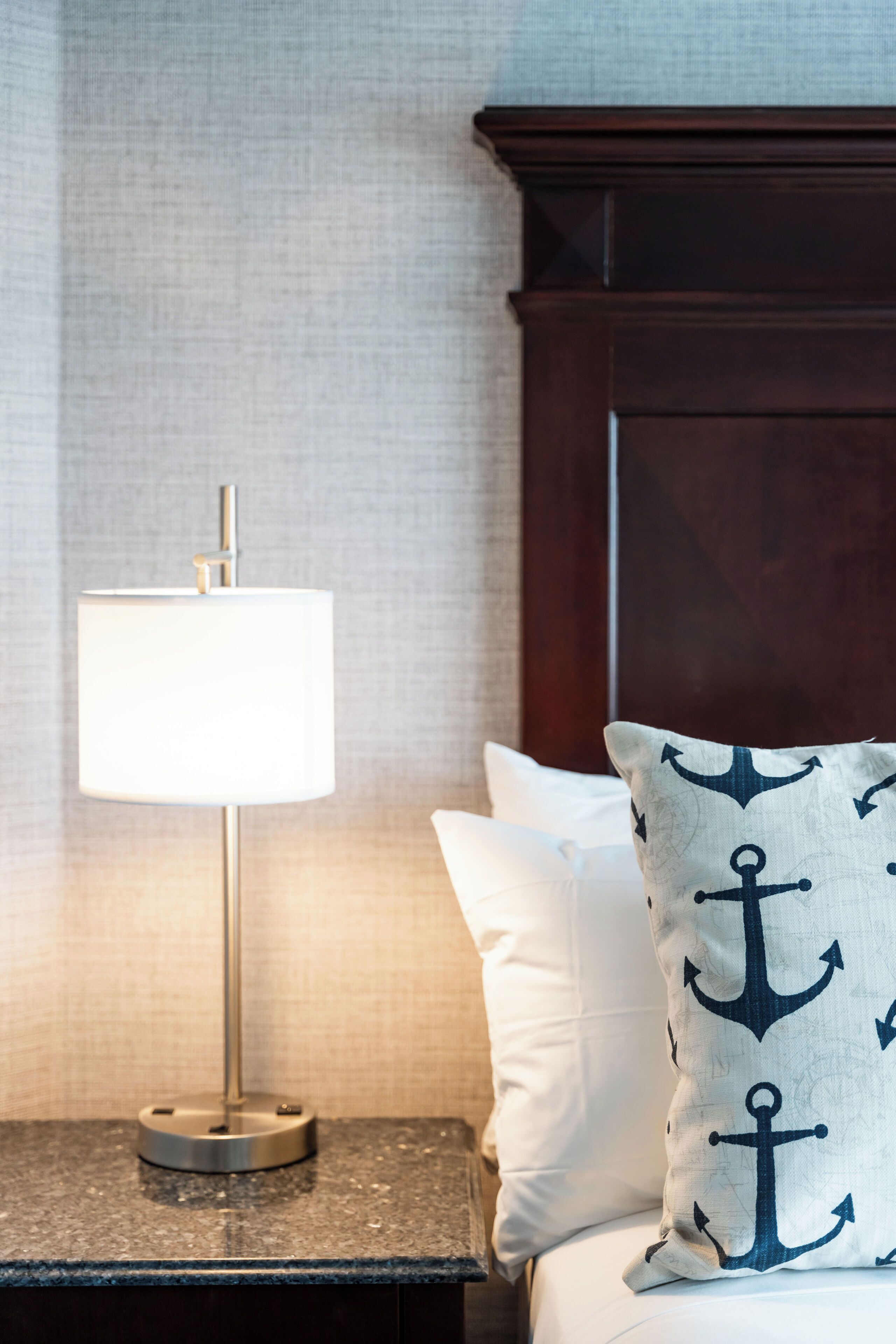 A neatly made bed with white linens and a pillow featuring an anchor pattern.