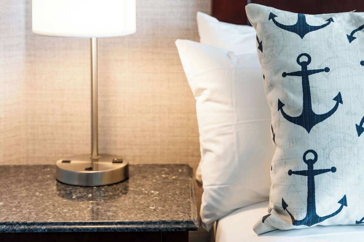 A neatly made bed with white linens and a pillow featuring an anchor pattern.