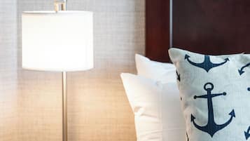A neatly made bed with white linens and a pillow featuring an anchor pattern.
