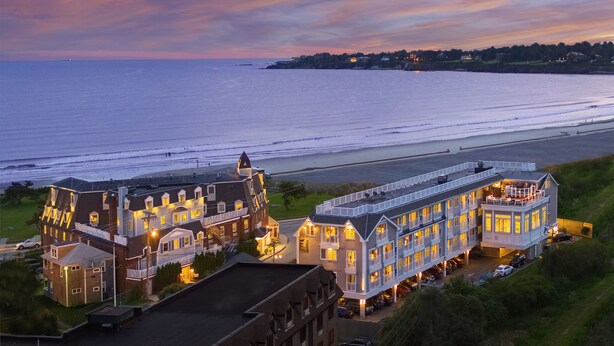 Un hotel frente al mar con varias construcciones, vistas a la playa y un aparcamiento.
