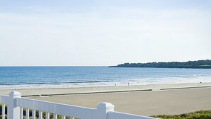 Una playa con una valla blanca en primer plano y una vista despejada del océano.