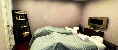 A hotel room with two beds, a TV mounted on the wall, and a small table with toiletries.