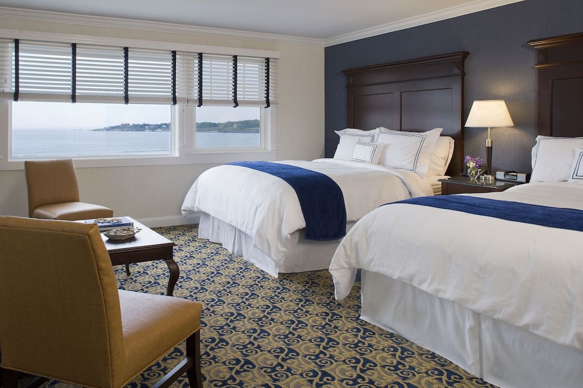 Une chambre d’hôtel avec deux lits, un bureau, une chaise, une lampe et une vue sur la mer.