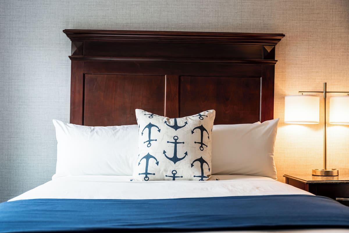 Un lit bien fait, avec une tête de lit en bois foncé, des oreillers blancs et une couvre-lit bleue.