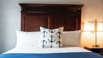 Una cama bien hecha con un cabecero de madera oscura, almohadas blancas y una colcha azul.