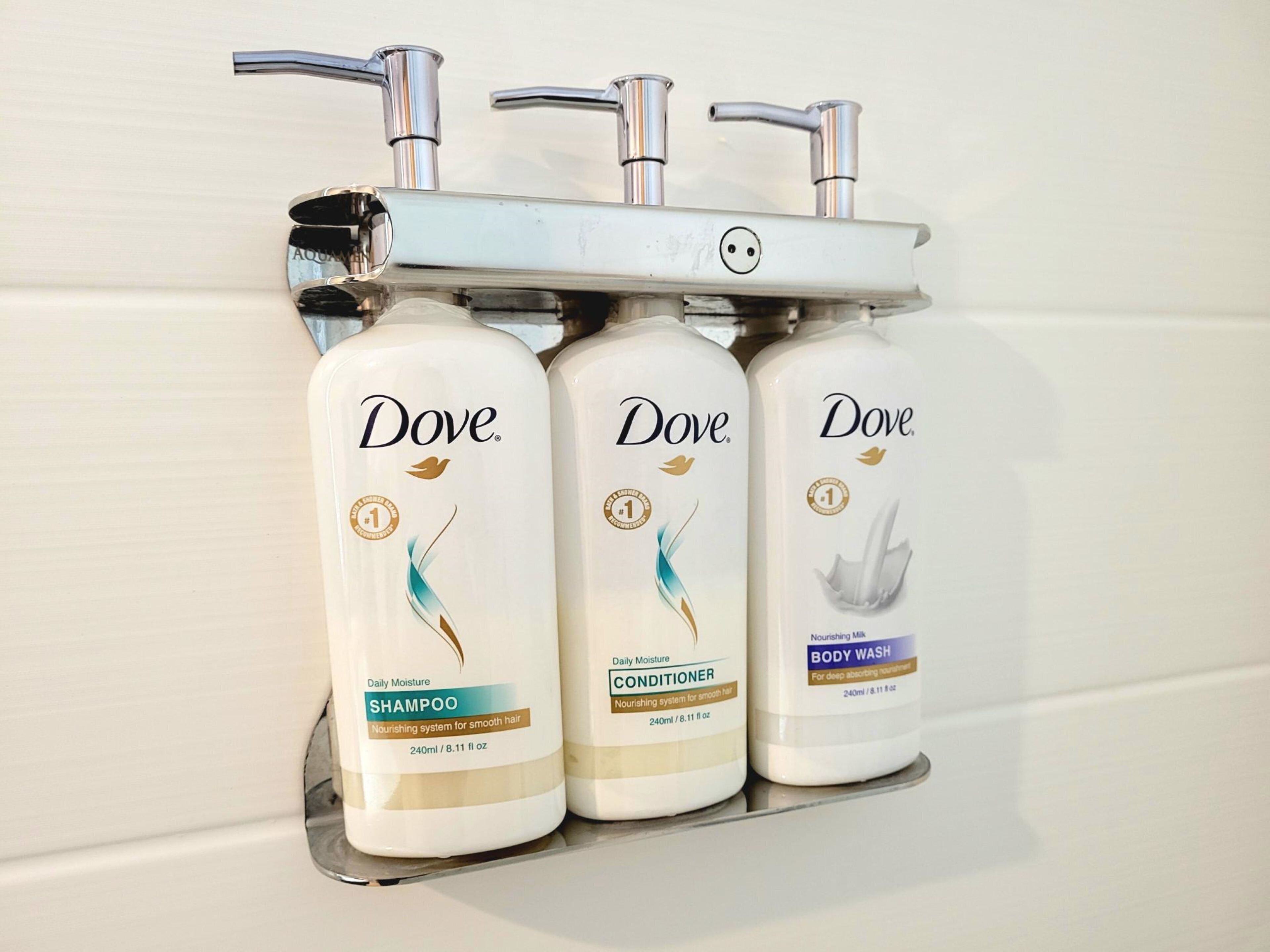 Três produtos de higiene pessoal Dove em um dosador fixado na parede.