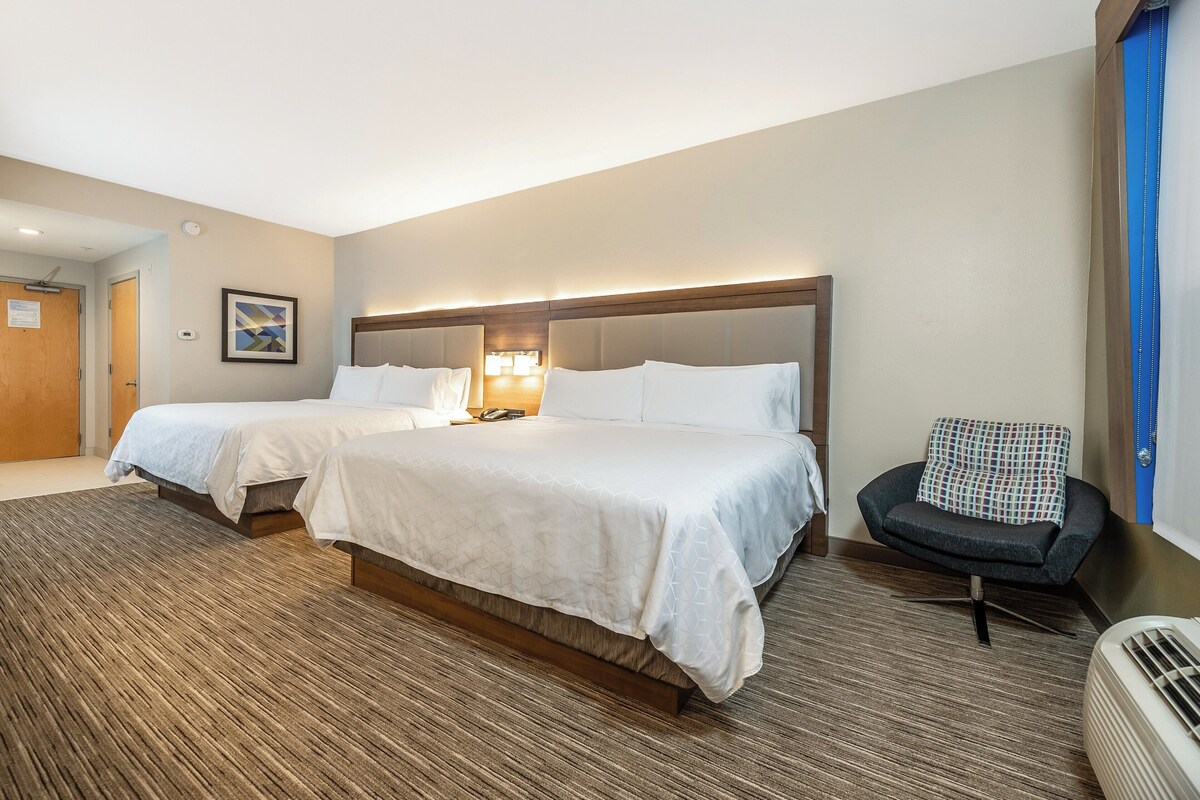 A hotel room with two beds, a chair, a heater, and a door.