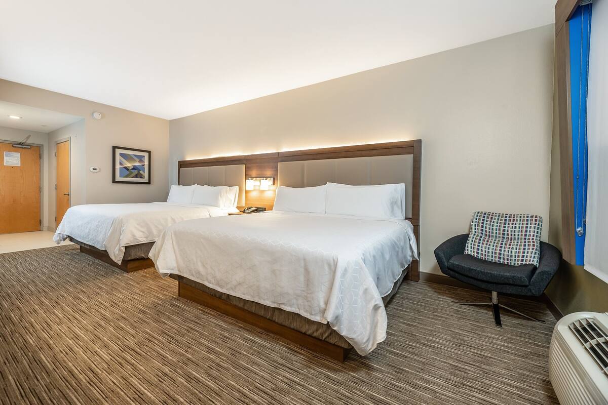 A hotel room with two beds, a chair, a heater, and a door.