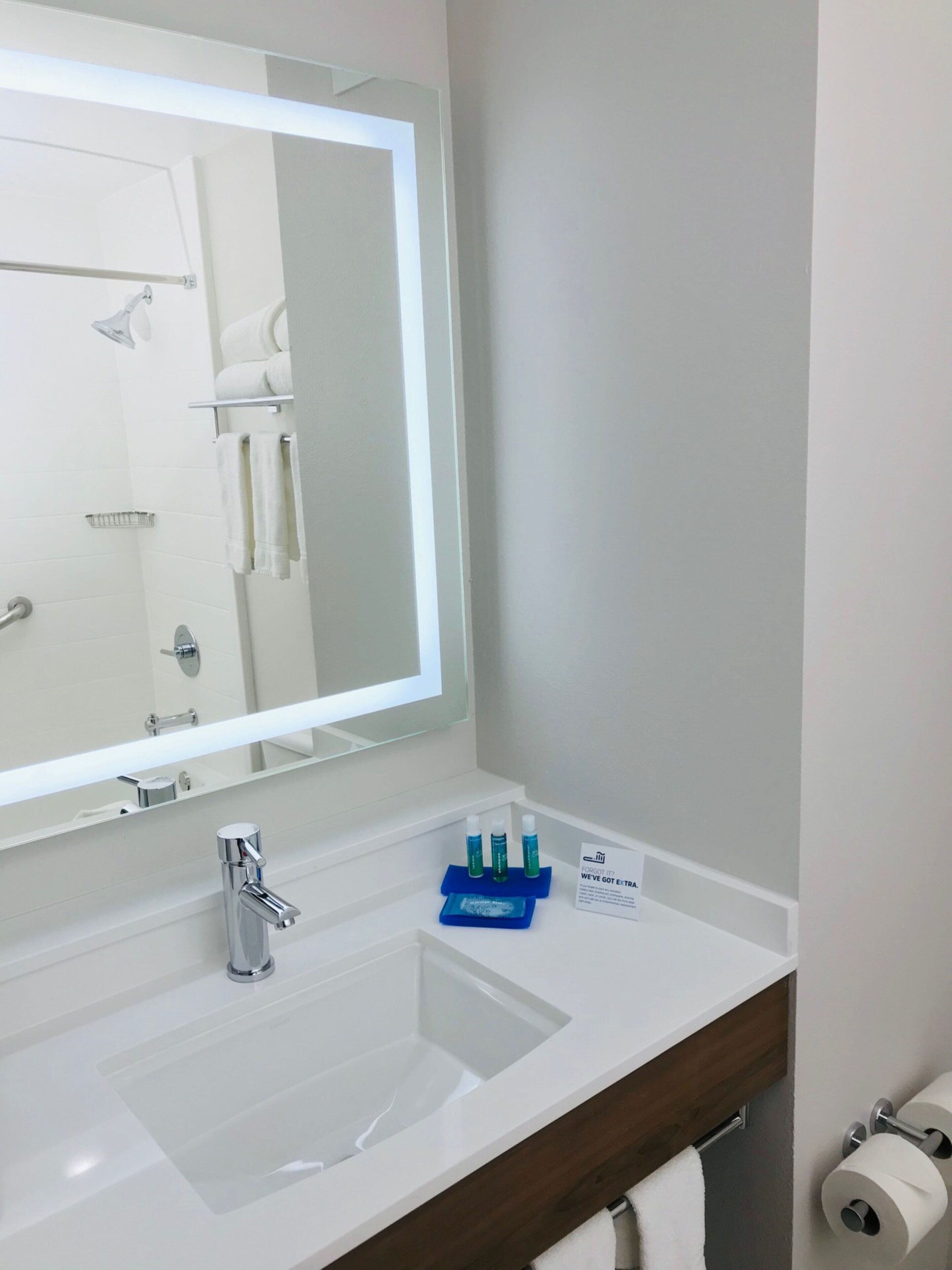 Un baño con lavamanos blanco, un espejo, toallero y un letrero que indica servicios adicionales.