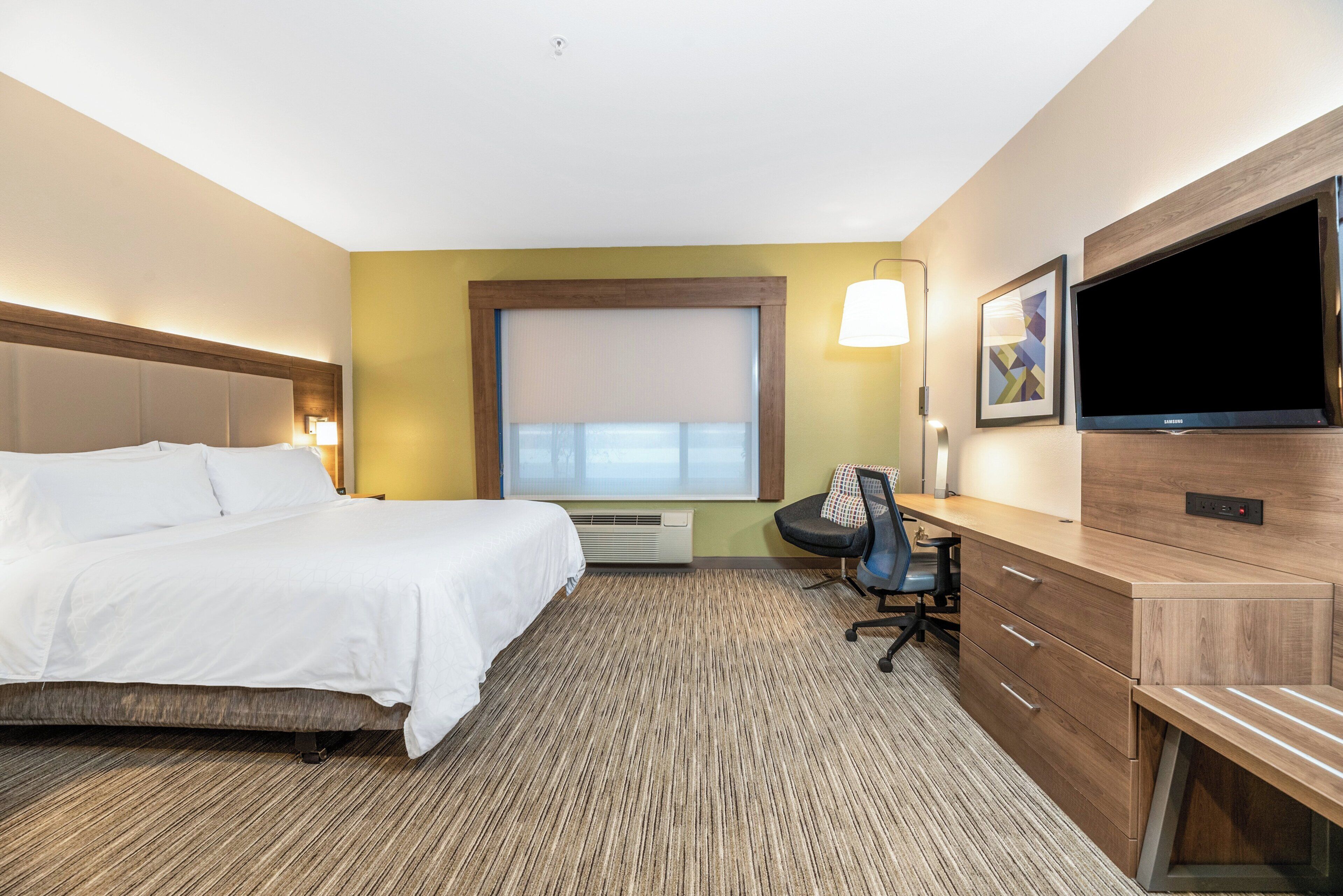 A hotel room with a bed, desk, chair, TV, and a window with blinds.