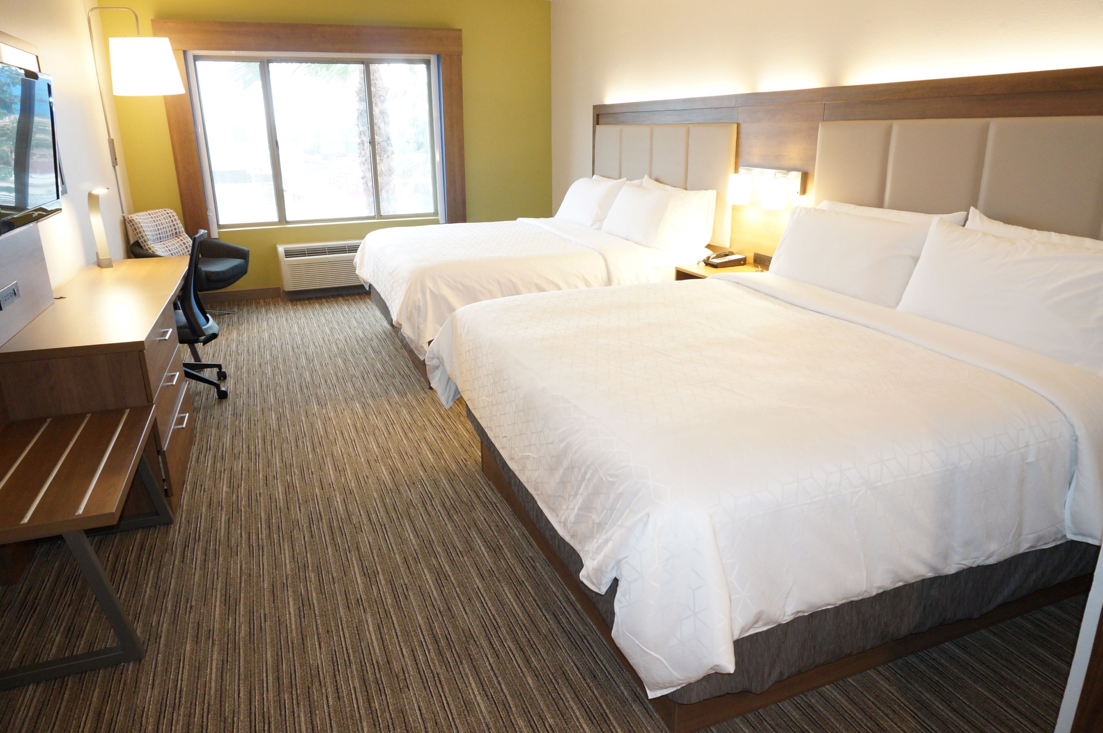 A hotel room with two beds, a desk, a chair, a TV, and a window.