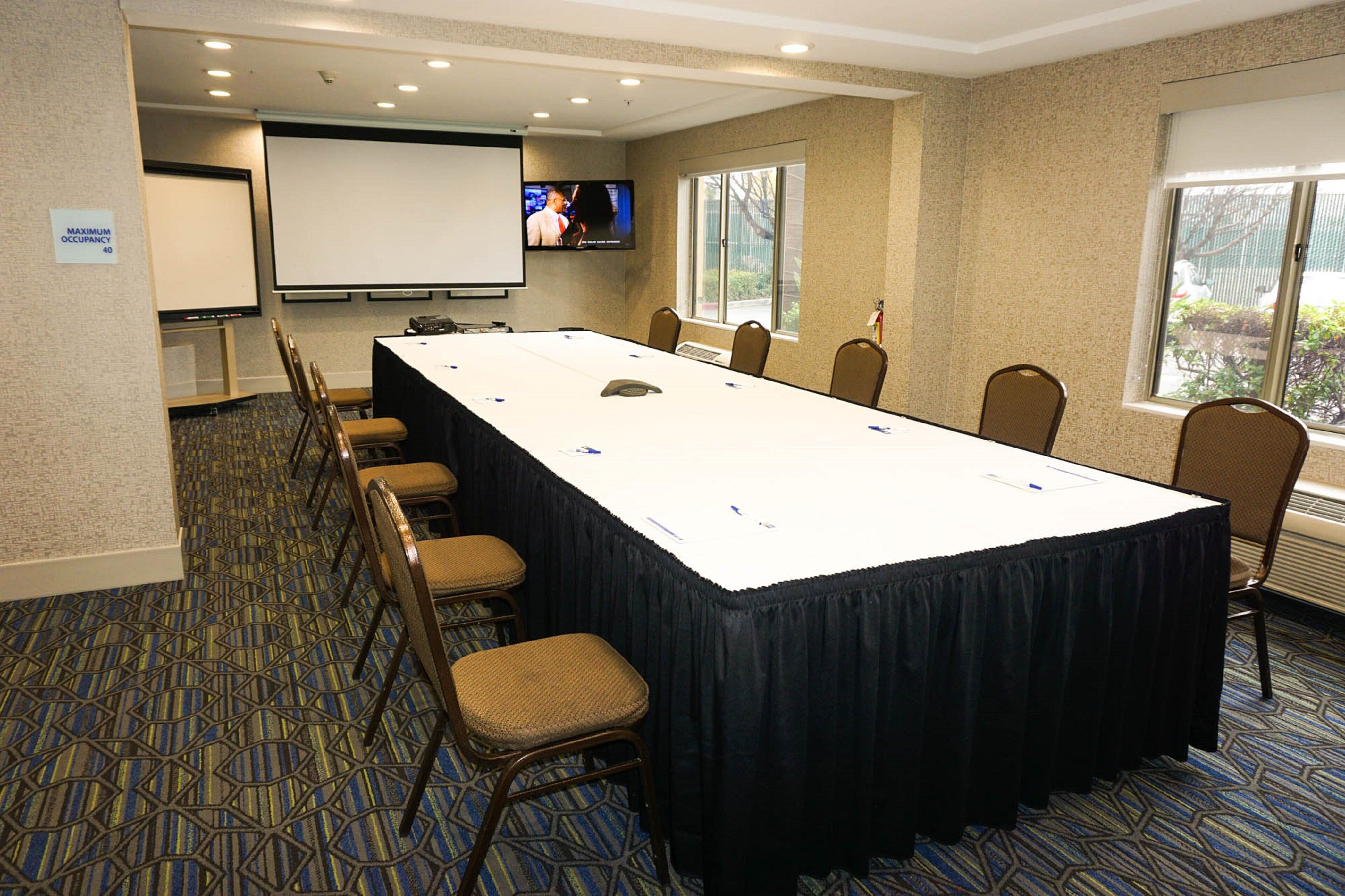 A conference room with a long table, chairs, a projector screen, and a television.