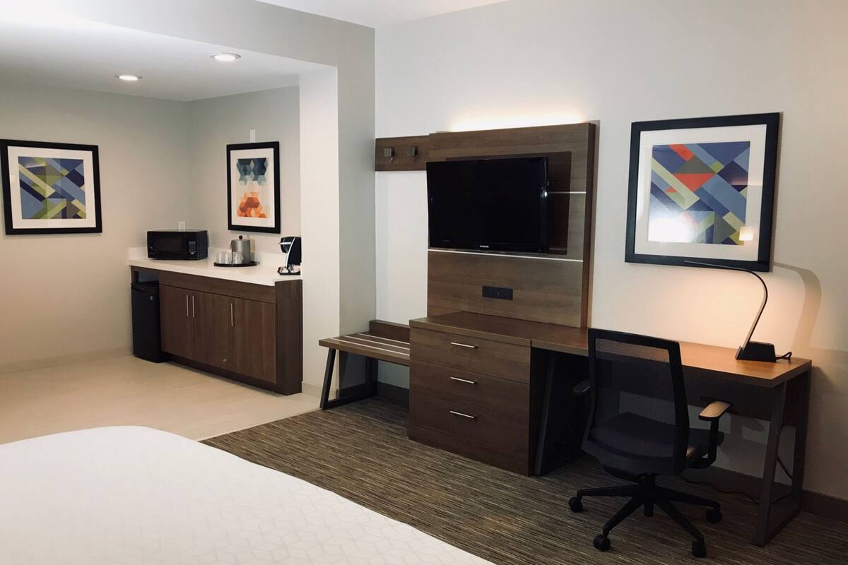 A hotel room with a bed, a desk with a chair, a TV, a microwave, and a coffee maker.