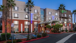 Ein Holiday Inn Express Gebäude mit modernem Design, einem Parkplatz und einem begrünten Eingangsbereich.