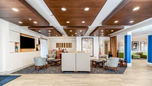 Eine moderne Lobby mit einer zentralen Sitzgruppe, einer Holzbalkendecke und einem gemusterten Teppich.