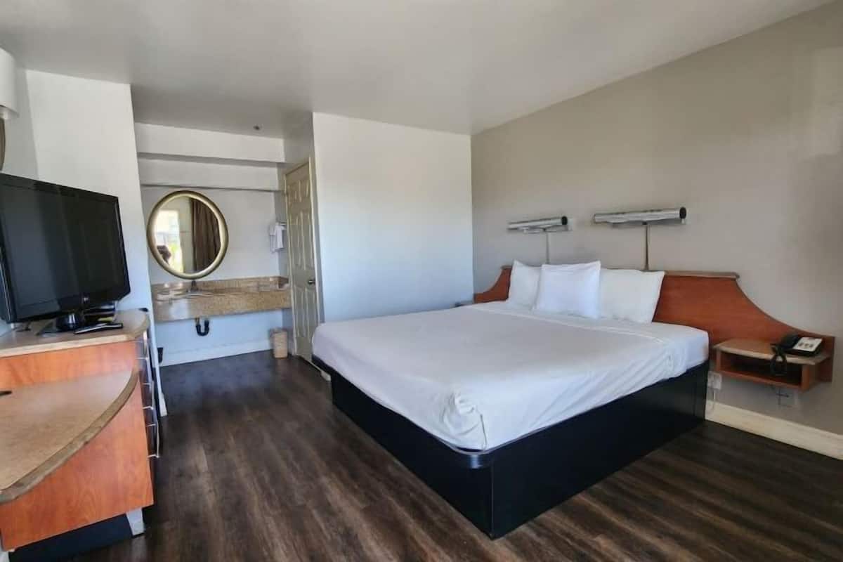 Ein Hotelzimmer mit Bett, Fernseher, Schreibtisch, Spiegel und Nachttisch.