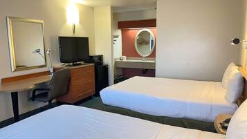 Une chambre d’hôtel avec deux lits, un bureau avec un ordinateur, une télévision et un petit réfrigérateur.