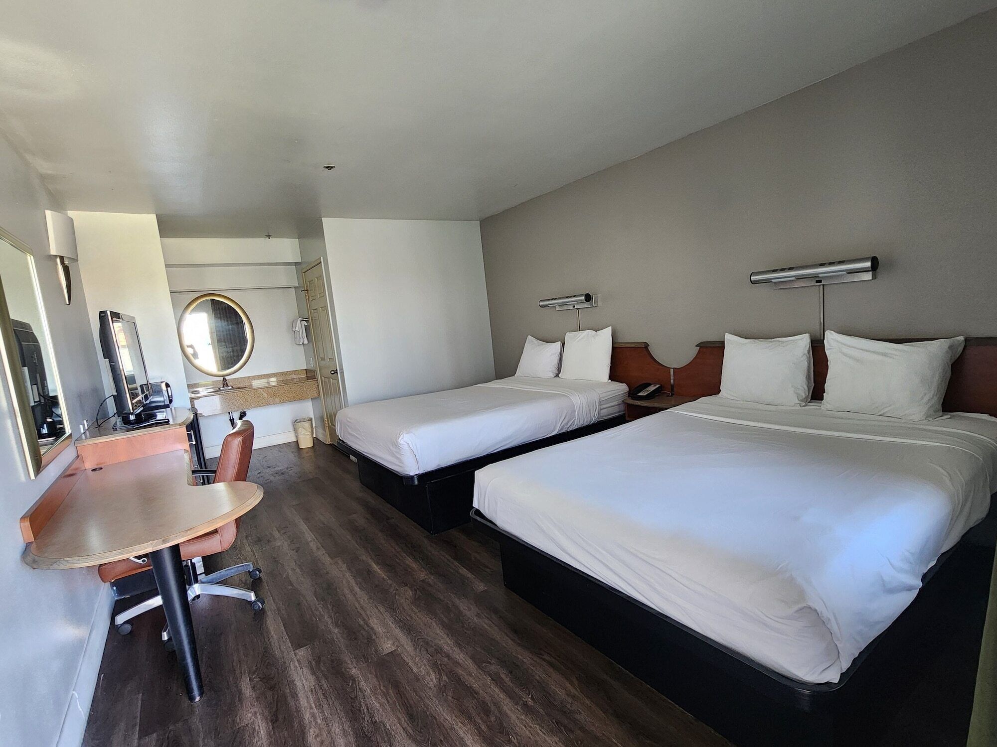 A hotel room with two beds, a desk, a chair, a mirror, and a small bathroom area.