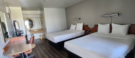 Une chambre d’hôtel avec deux lits, un bureau, une chaise, un miroir et une petite salle de bain.
