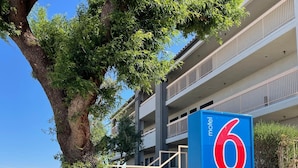 Ein Schild eines Motels mit rotem und blauem Logo, einem Baum und einem mehrstöckigen Gebäude im Hintergrund.