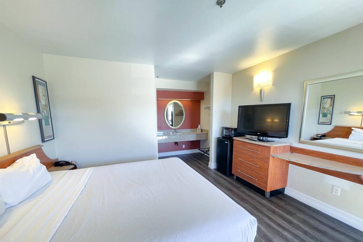 Ein Hotelzimmer mit zwei Betten, einem Fernseher, einer Minibar und einem Spiegel.