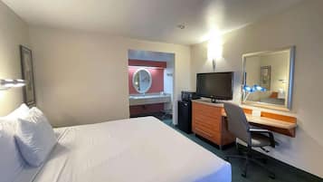 A hotel room with a bed, a desk with a computer, a television, a mirror, and a small kitchenette.