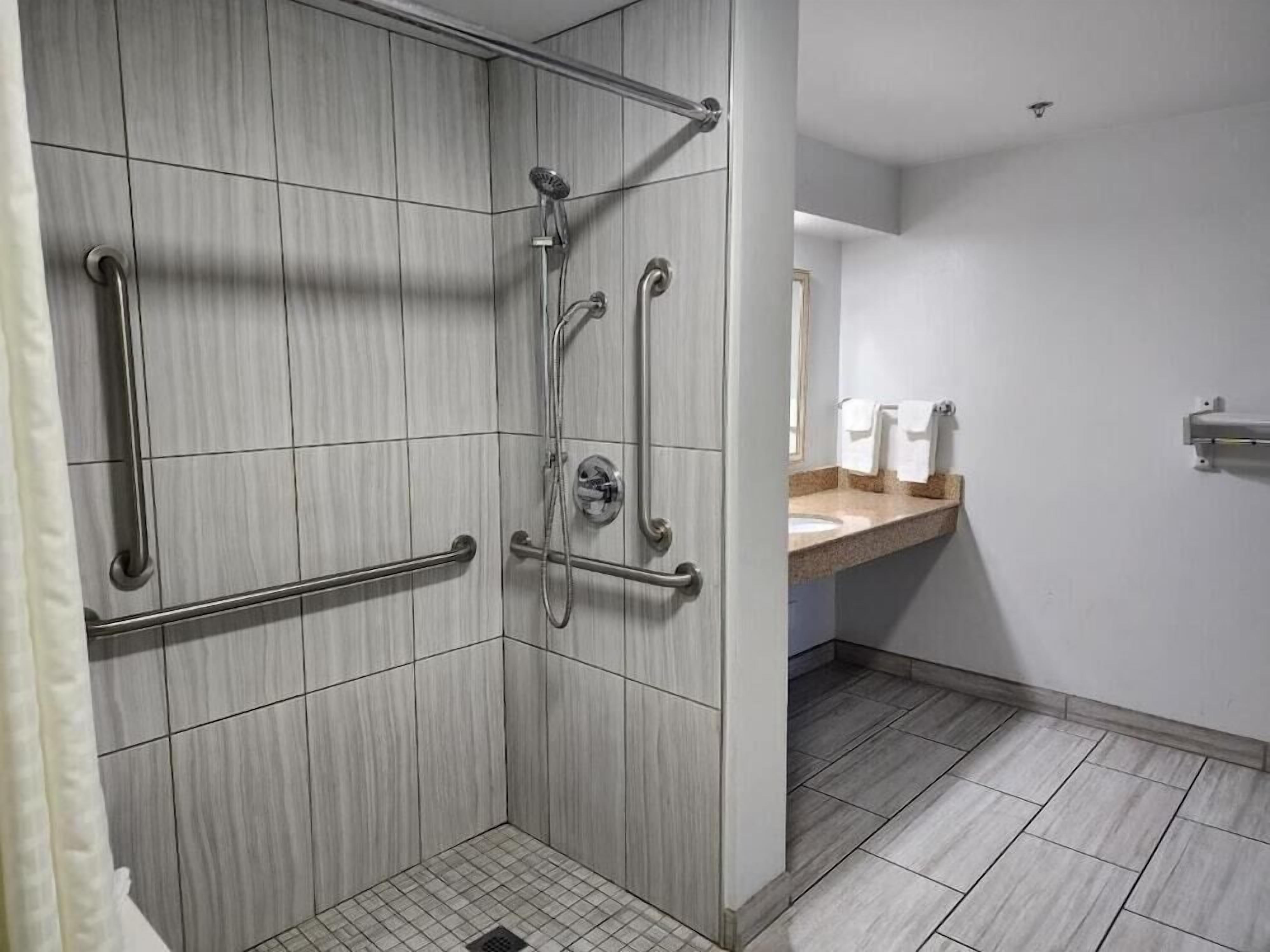 A modern bathroom with a walk-in shower, grab bars, and a vanity with a sink and towel rack.