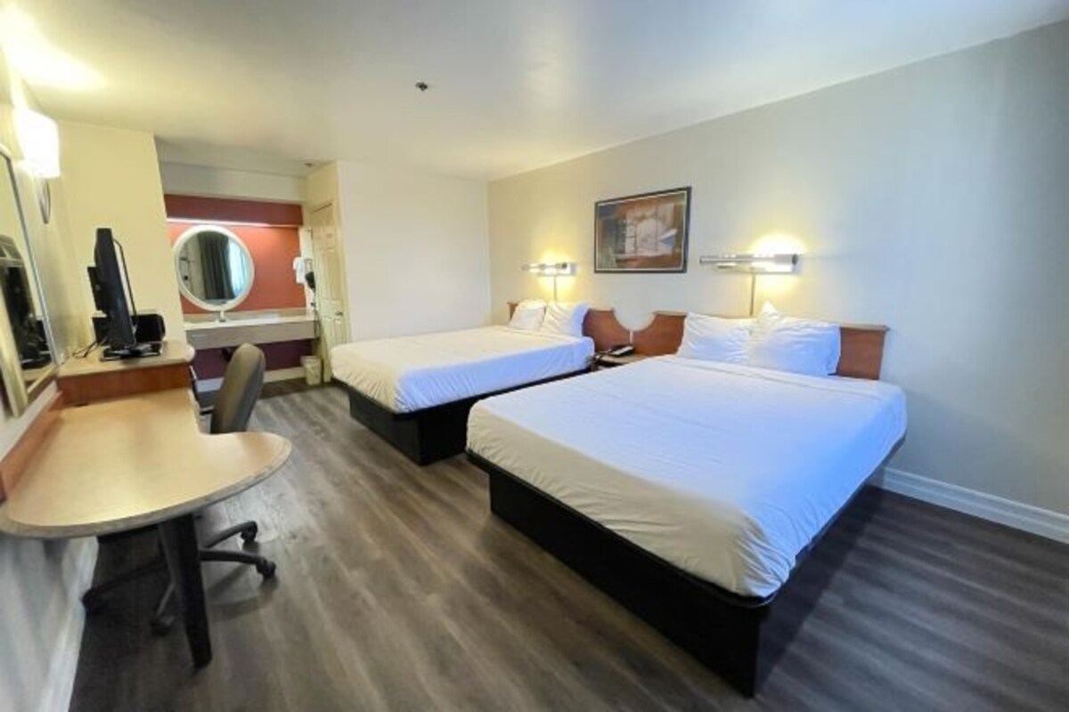 Een hotelkamer met twee bedden, een bureau, een stoel, een spiegel en een schilderij aan de muur.