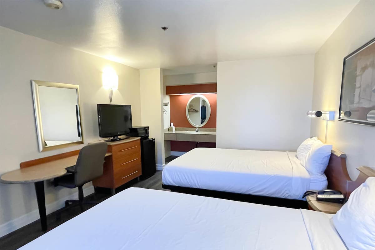 Ein Hotelzimmer mit zwei Betten, einem Schreibtisch mit Computer, einem Fernseher und einem Spiegel.
