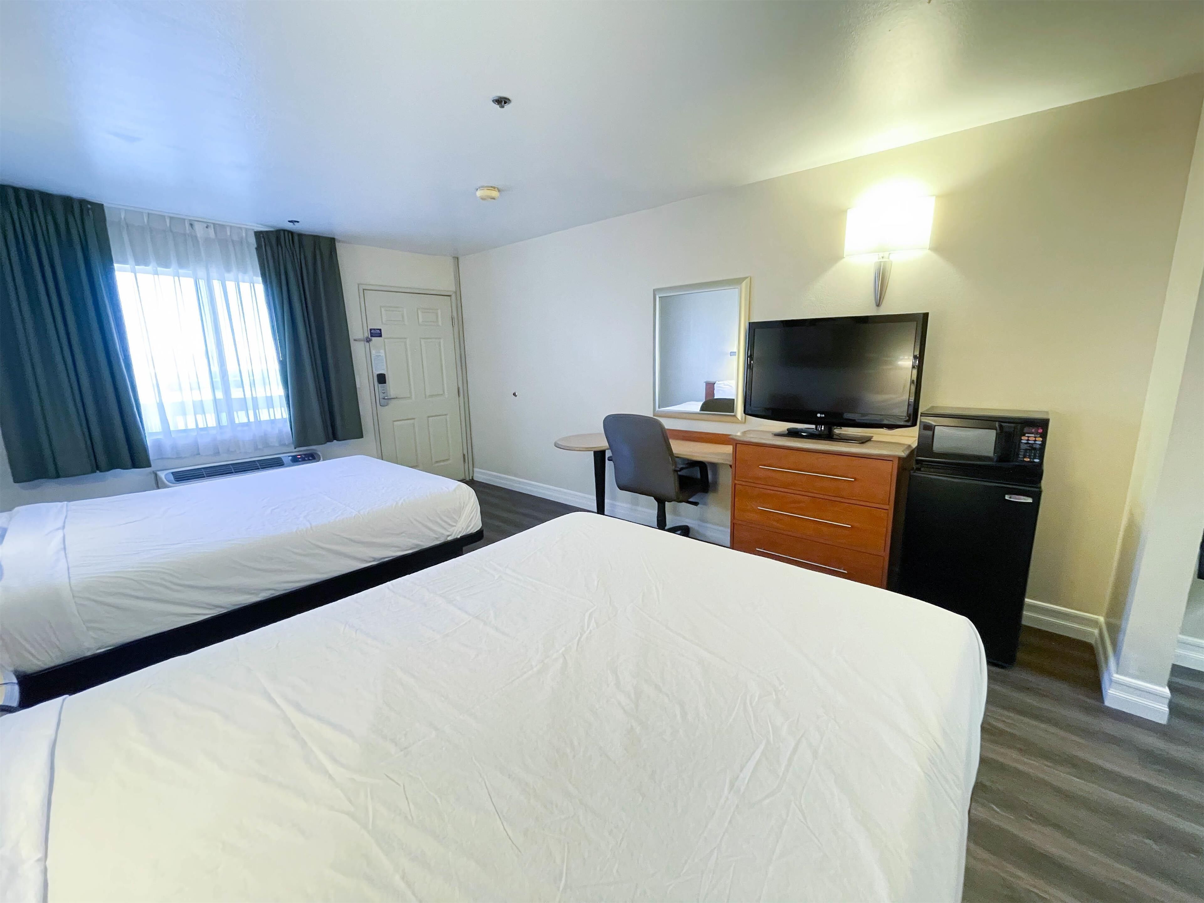 A hotel room with two beds, a desk with a computer and a microwave, and a window with curtains.