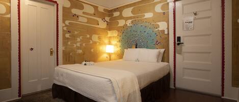 A hotel room with a bed, a nightstand, a wall clock, and a door with a red trim.