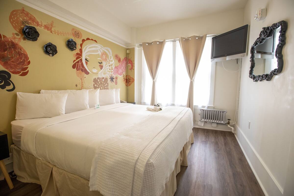 A neatly made bed with white linens, a wall-mounted TV, and a radiator.
