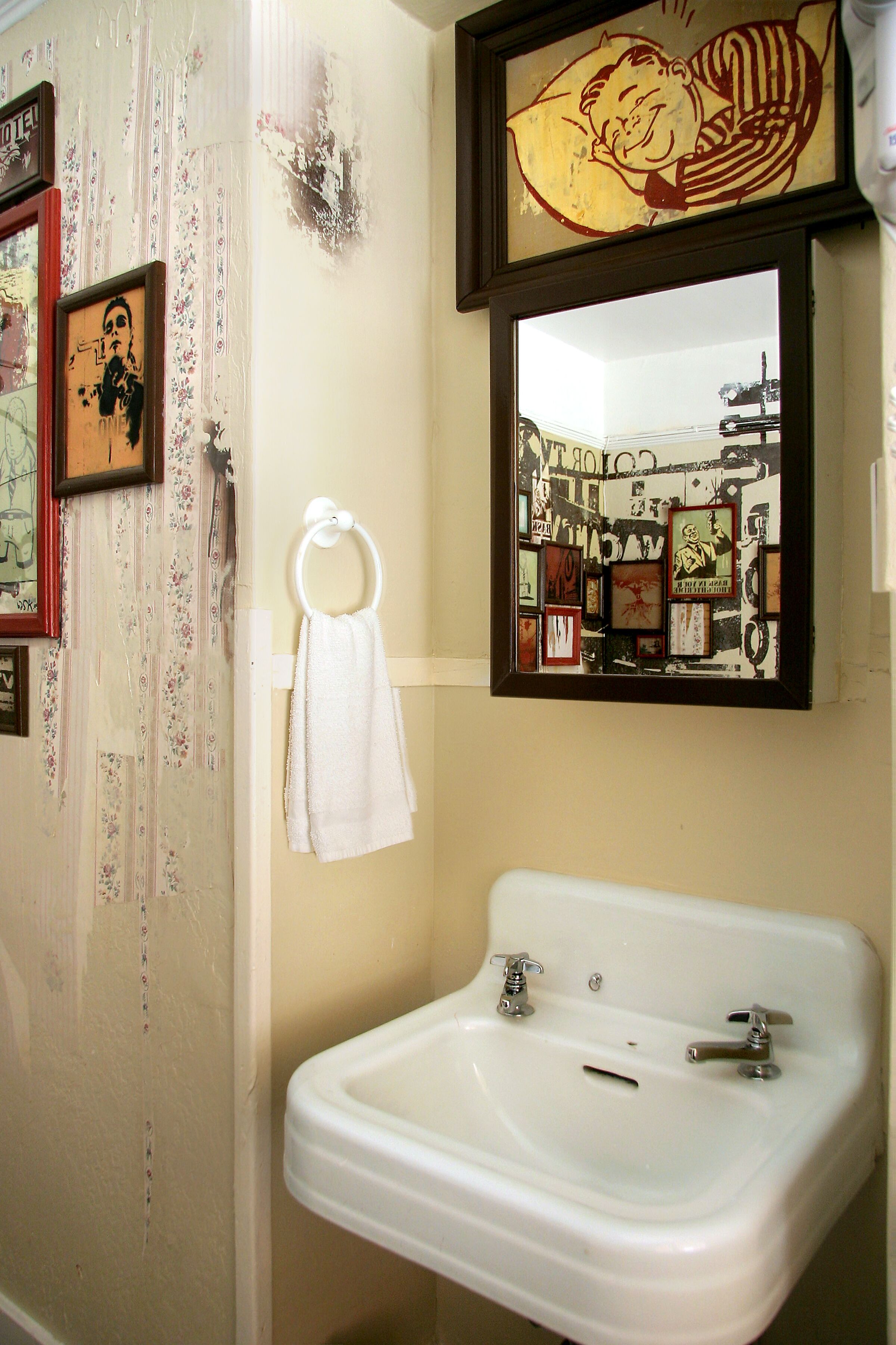 Un baño con un lavamanos blanco, un aro para toallas y un espejo con un collage de fotos.
