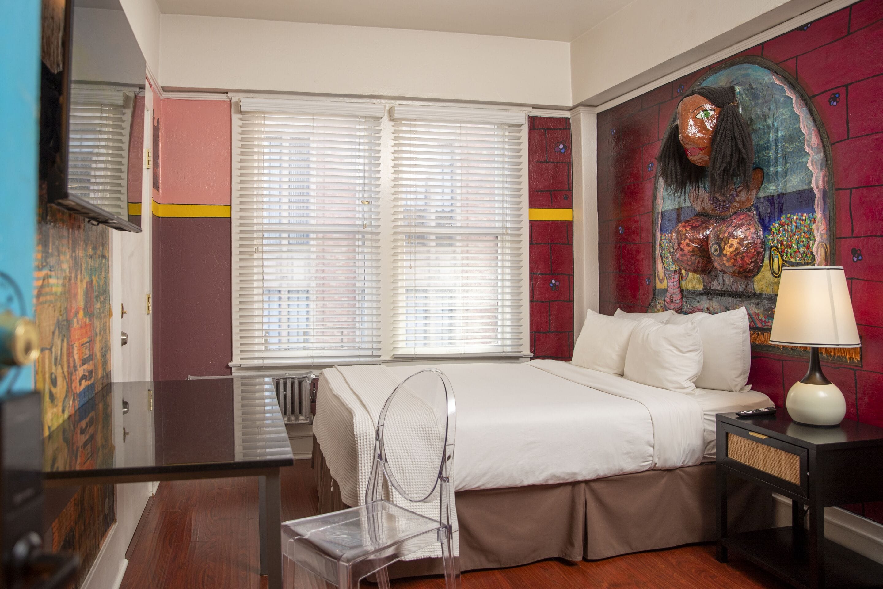 A hotel room with a bed, a desk, a chair, and a window with blinds.
