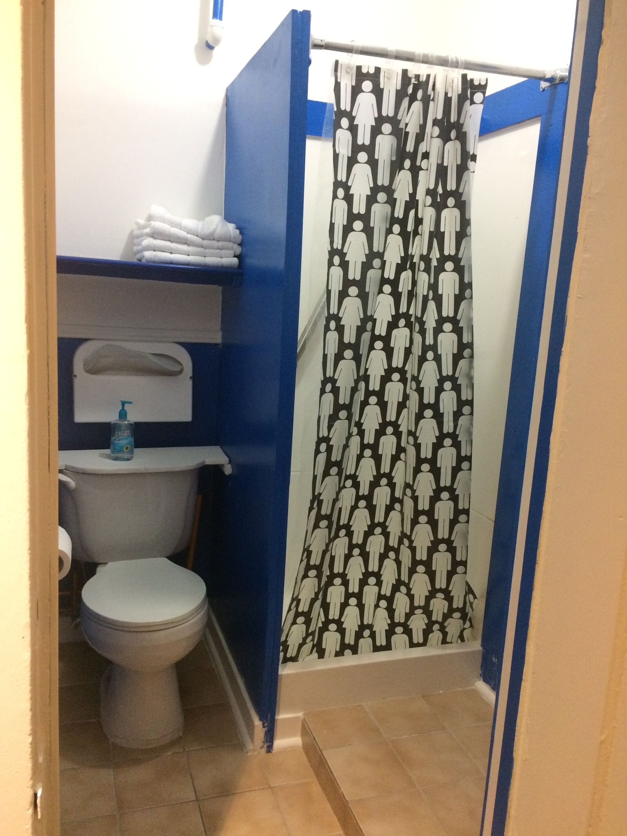 A bathroom with a toilet, a shelf with folded towels, and a shower curtain with a pattern of human figures.