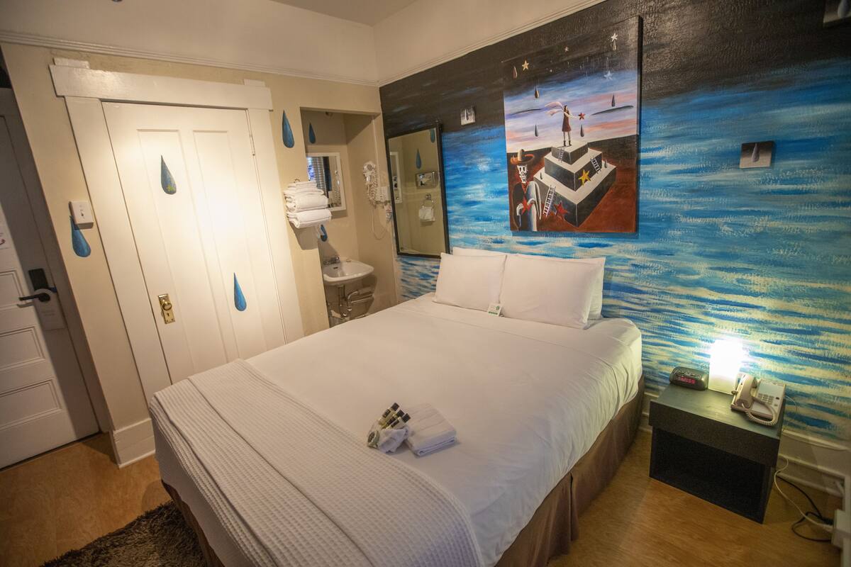 A hotel room with a large bed, a nightstand with a phone, and a painting on the wall.