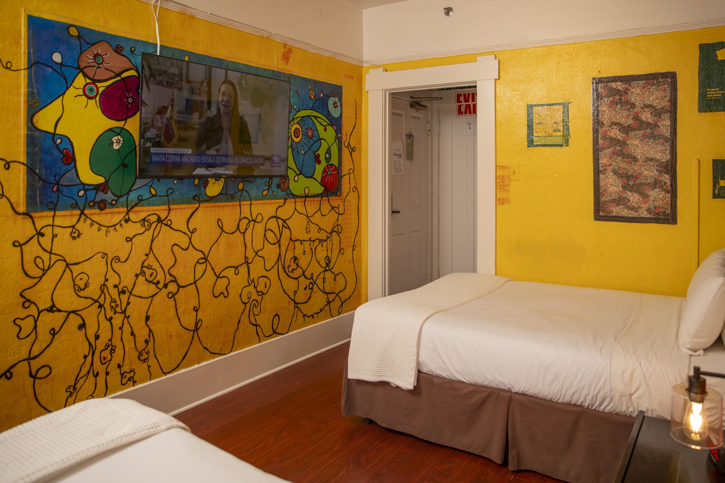 A hotel room with a bed, a television mounted on the wall, and a door leading to another room.