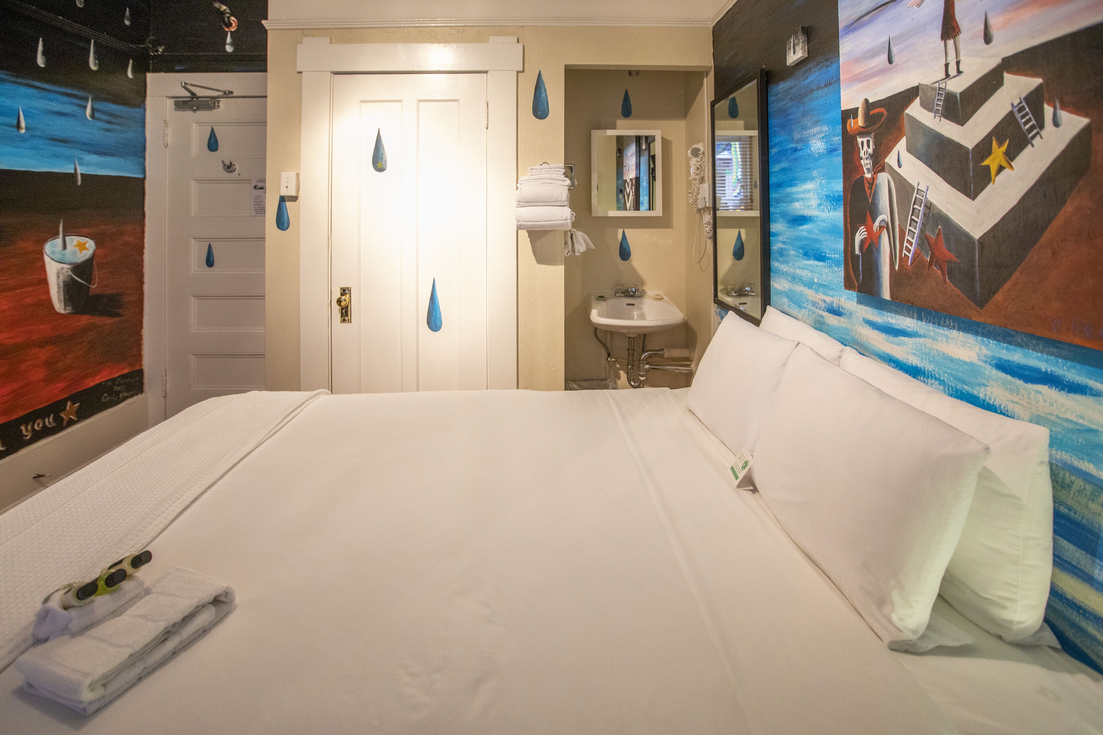 Habitación de hotel con una cama grande, baño con lavamanos y espejo, y un mural en la pared.