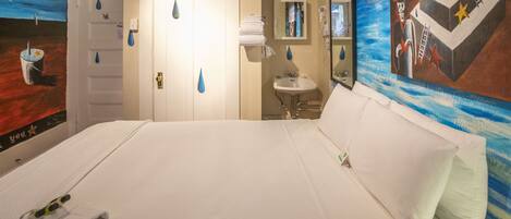 Habitación de hotel con una cama grande, baño con lavamanos y espejo, y un mural en la pared.