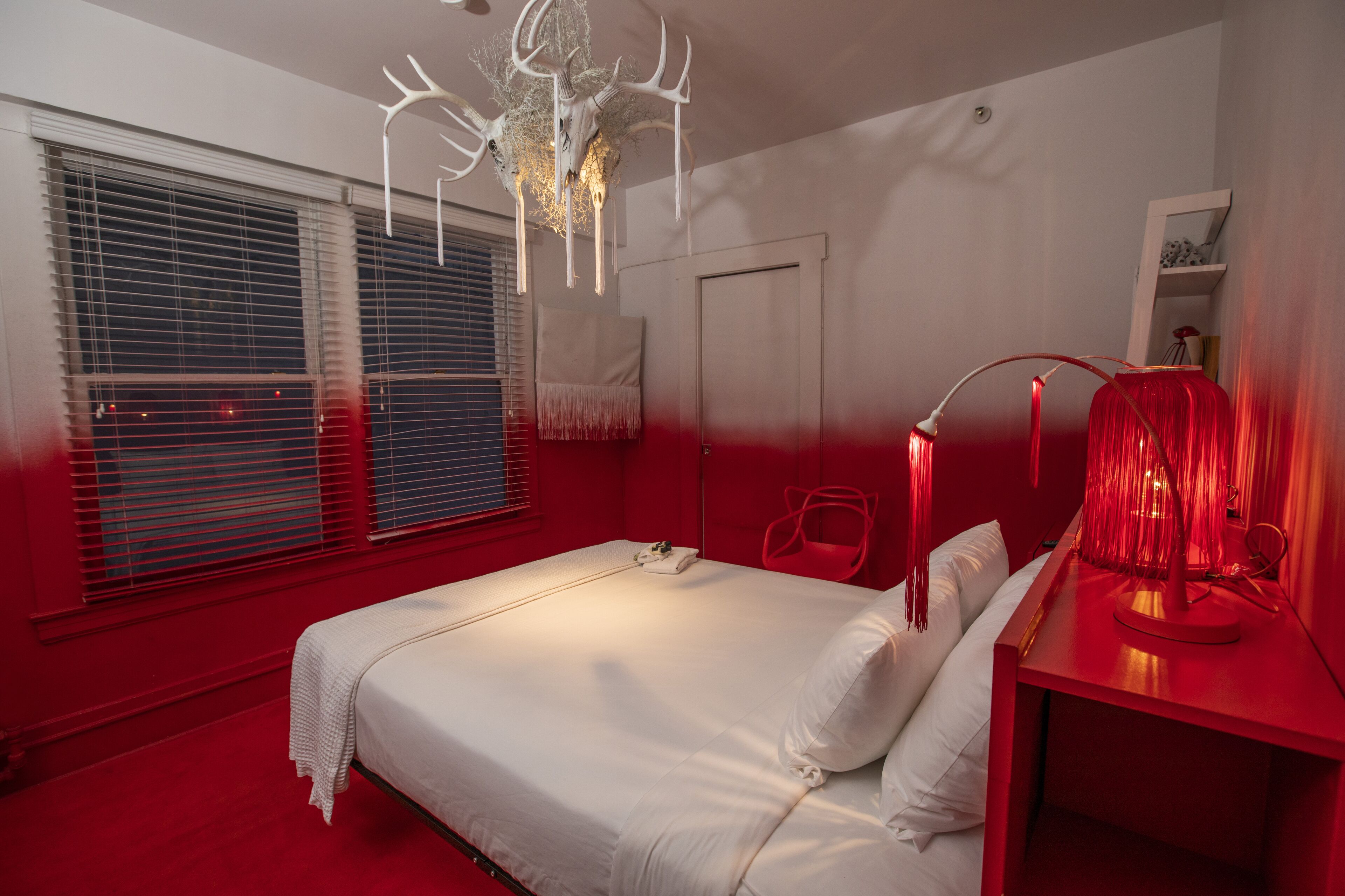 A bedroom with a large bed, a red nightstand, a white lamp, and a unique ceiling light fixture.